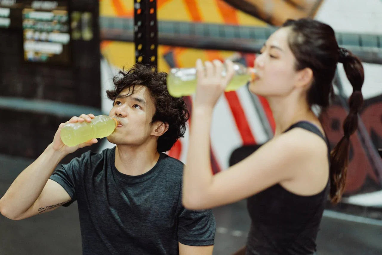 A man and a female drinking an electrolyte drink while sweating