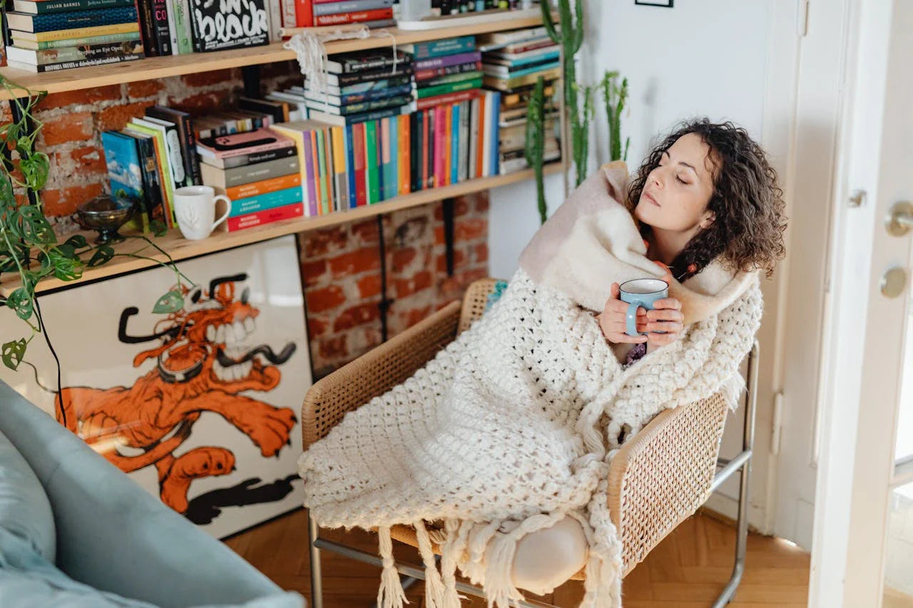 A woman cold with curly hair wrapped in a shawl, enjoying tea in a cozy home environment