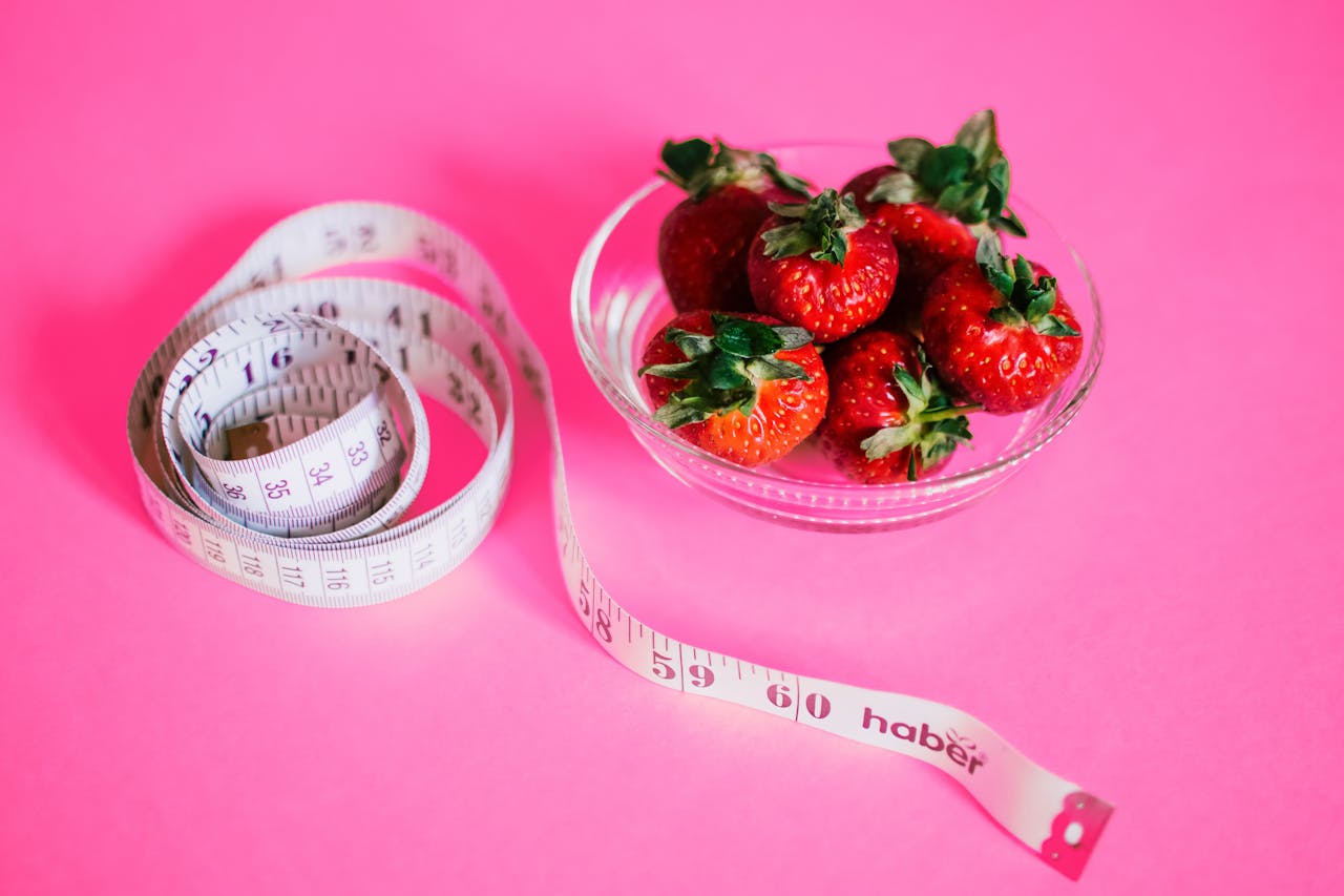 strawberries in a glass bowl with a tape scale next to them - All on a pink background