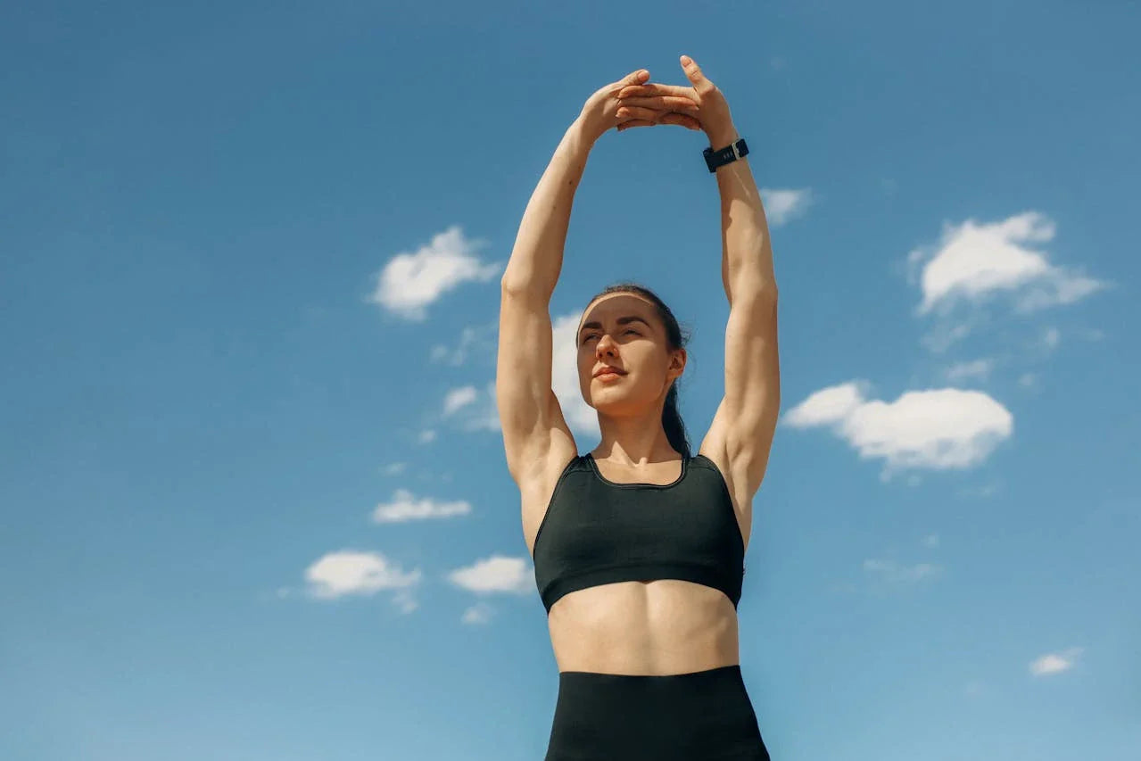 Woman in sports bra stretching under a clear blue sky, embodying fitness and wellness